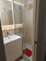 Detail of bathroom basin on drawer vanity, backlit mirror and glass shower with red mat